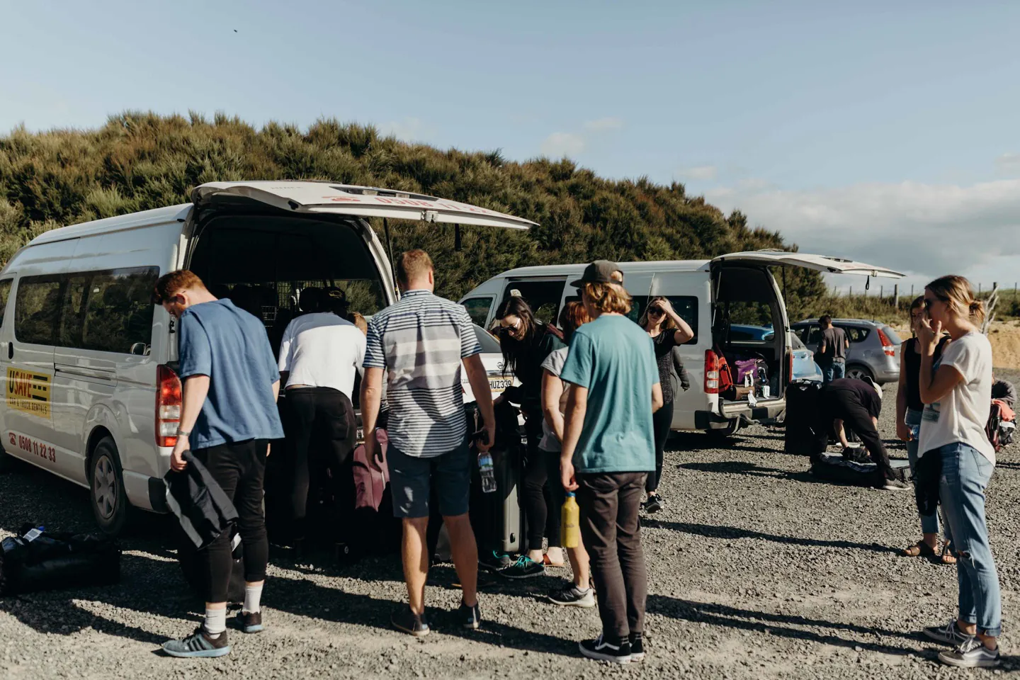 A group gathering beside open vans on a sunny coastal outing.