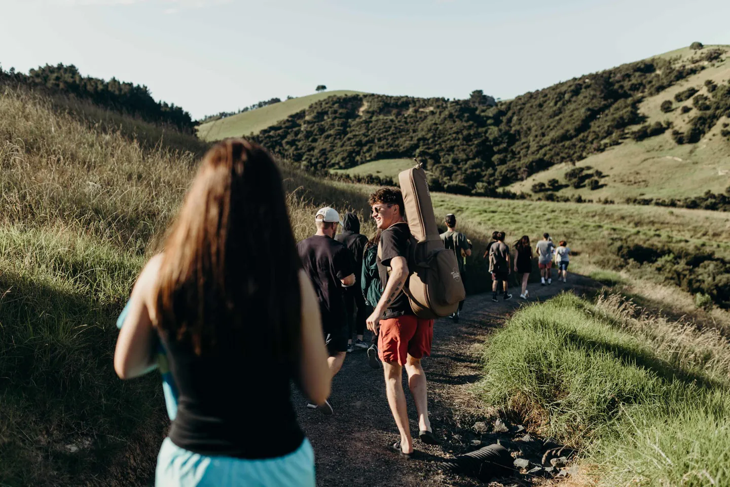 A group walking together along a grassy track, with a guitar carried on one person’s back.