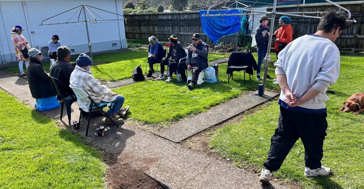 People seated and standing together at a backyard gathering beside a house.