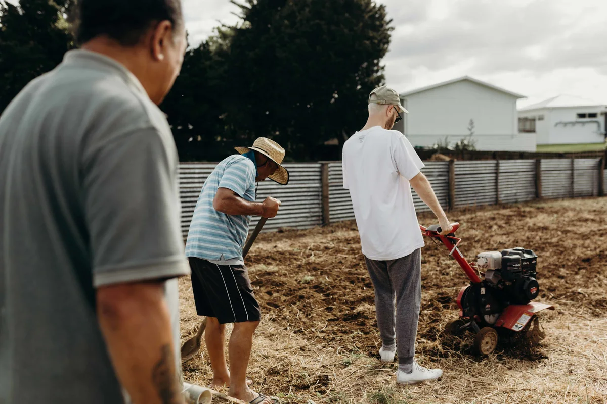 Three people working the soil together with a spade and garden tiller.